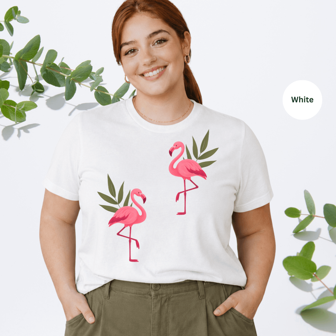 White Bella+Canvas 3001 t-shirt with two hand-painted pink flamingos and tropical leaves graphic